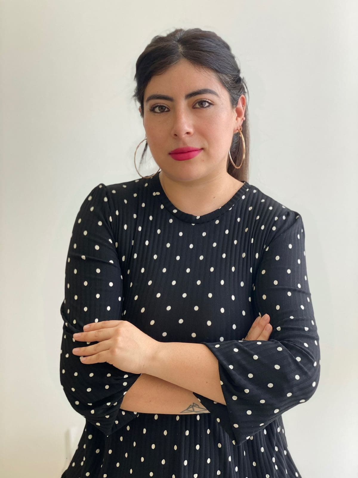 Woman wearing a black polka dot dress and pink lipstick with her arms crossed.